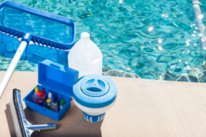 Image of pool cleaning and testing equipment next to a clear blue pool