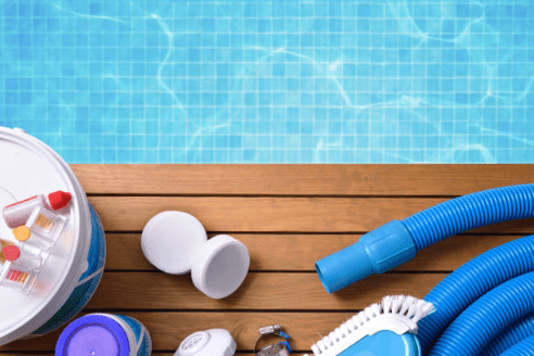 Image of pool cleaning supplies laid out by a crystal clear blue pool